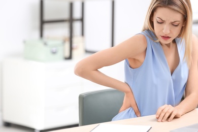 Photo of Young woman suffering from back pain in office