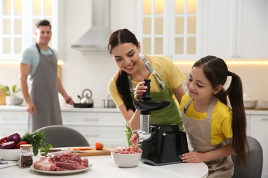 Photo of Happy family making dinner together in kitchen, mother and daughter using modern meat grinder
