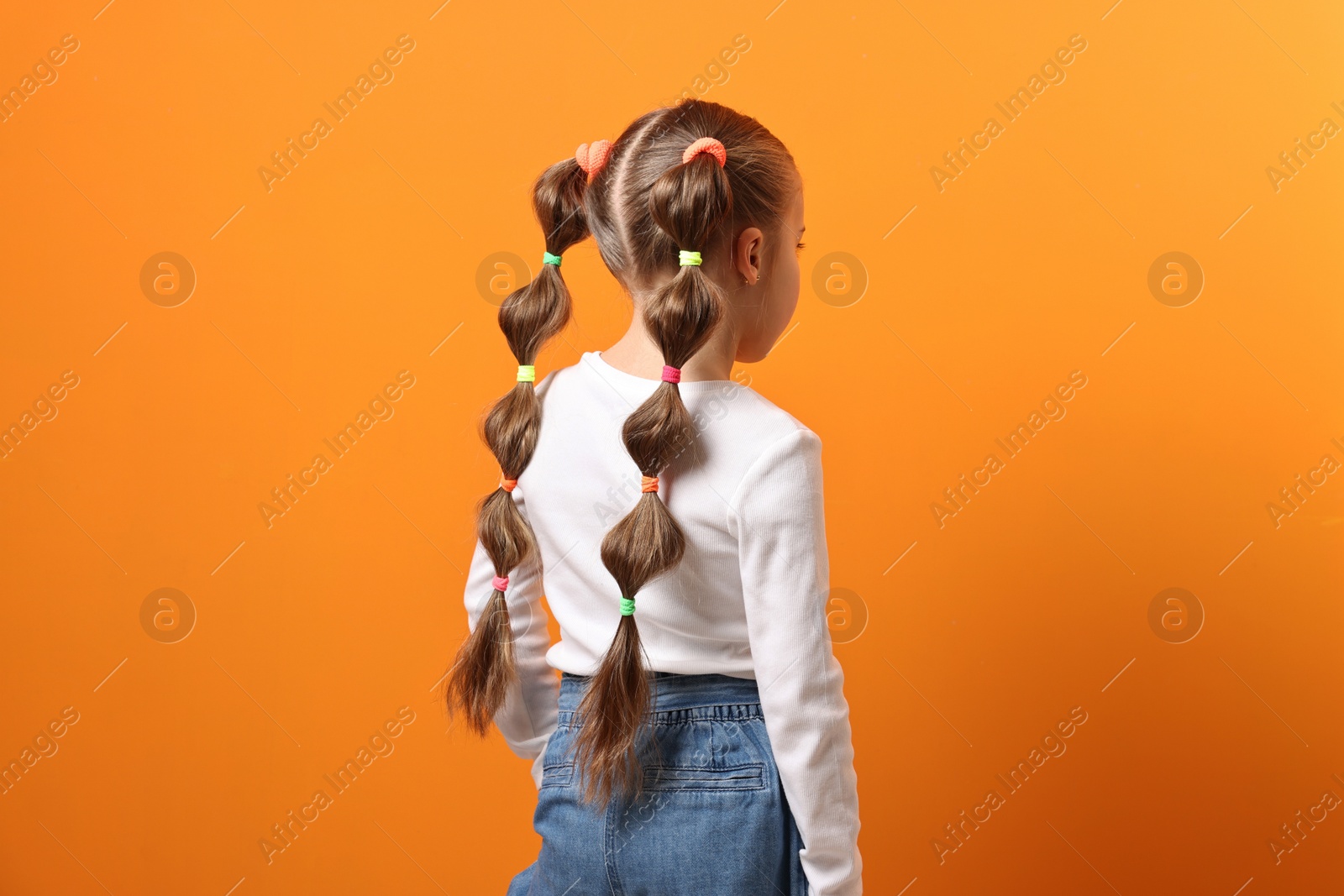 Photo of Little girl with beautiful hairstyle on orange background, back view
