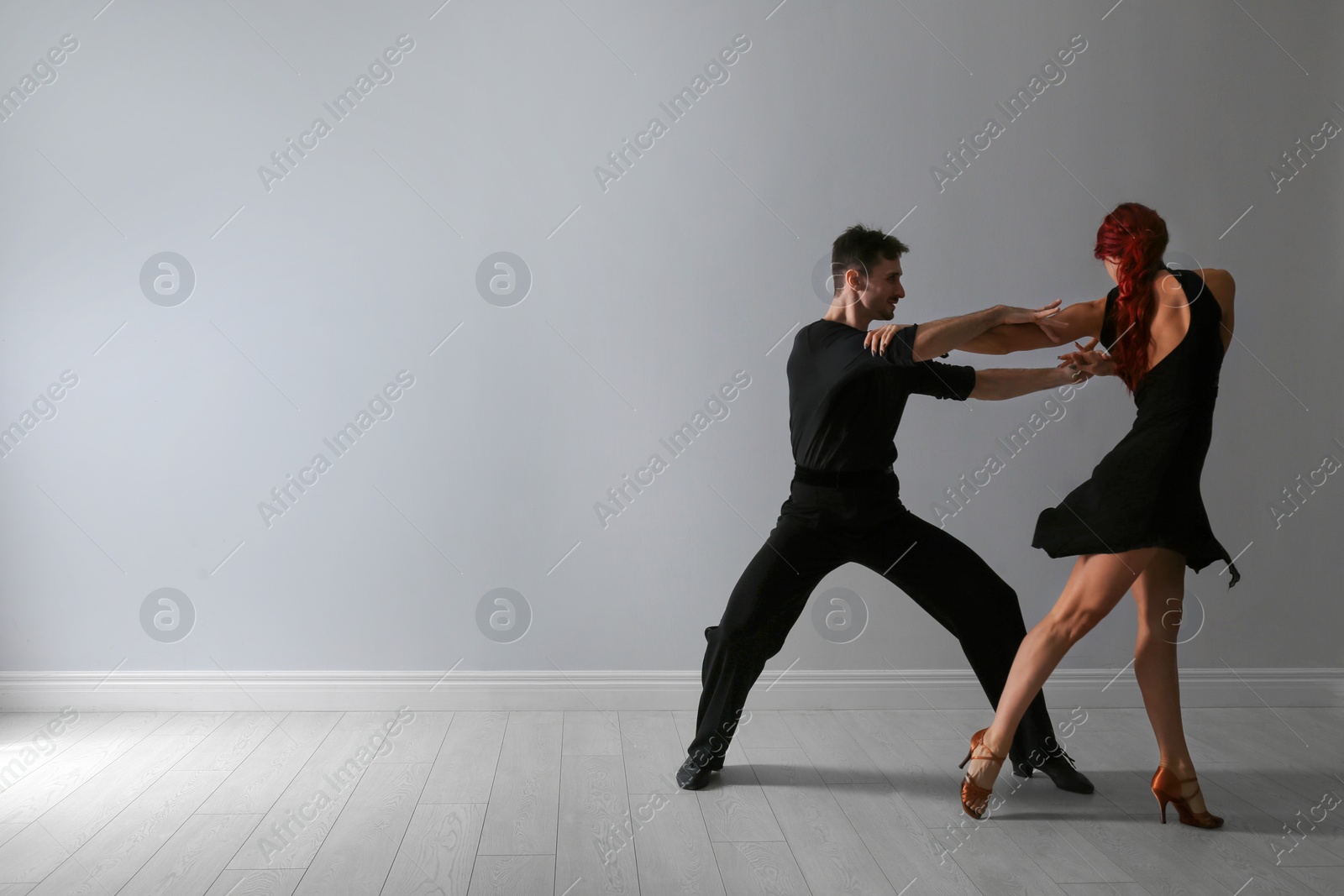 Photo of Beautiful young couple dancing near light wall. Space for text