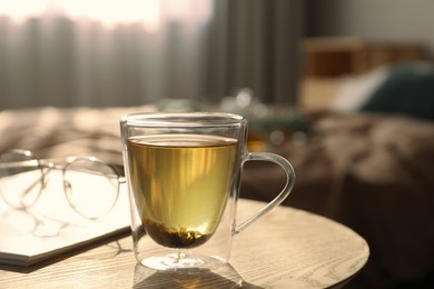 Glass cup of freshly brewed tea on wooden table in bedroom. Cozy home atmosphere