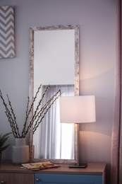 Photo of Large mirror and lamp on table indoors. Idea for home design