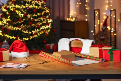 Santa's Claus workplace. Gift boxes, wrapping paper, letters on table and costume in room with Christmas tree