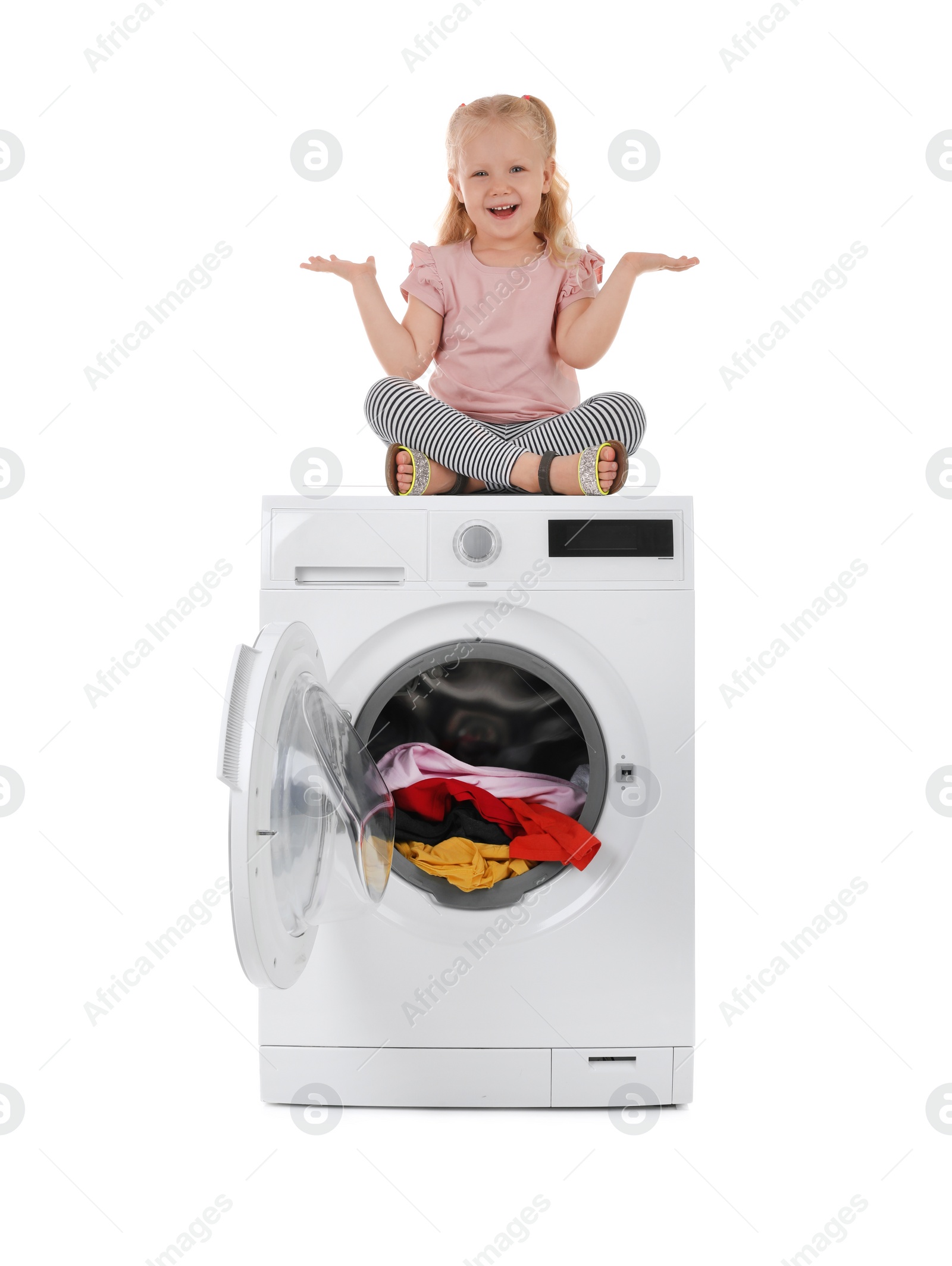 Photo of Cute little girl sitting on washing machine with laundry against white background