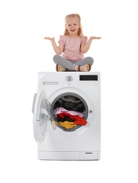 Cute little girl sitting on washing machine with laundry against white background