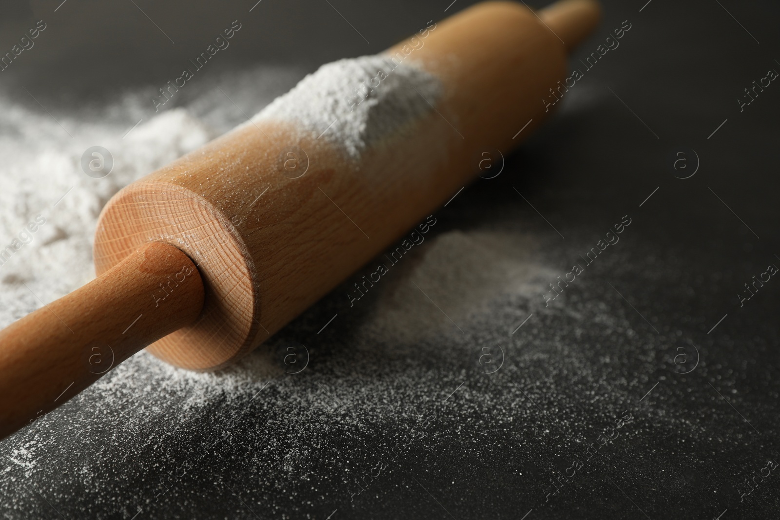 Photo of Scattered flour and rolling pin on black table, closeup