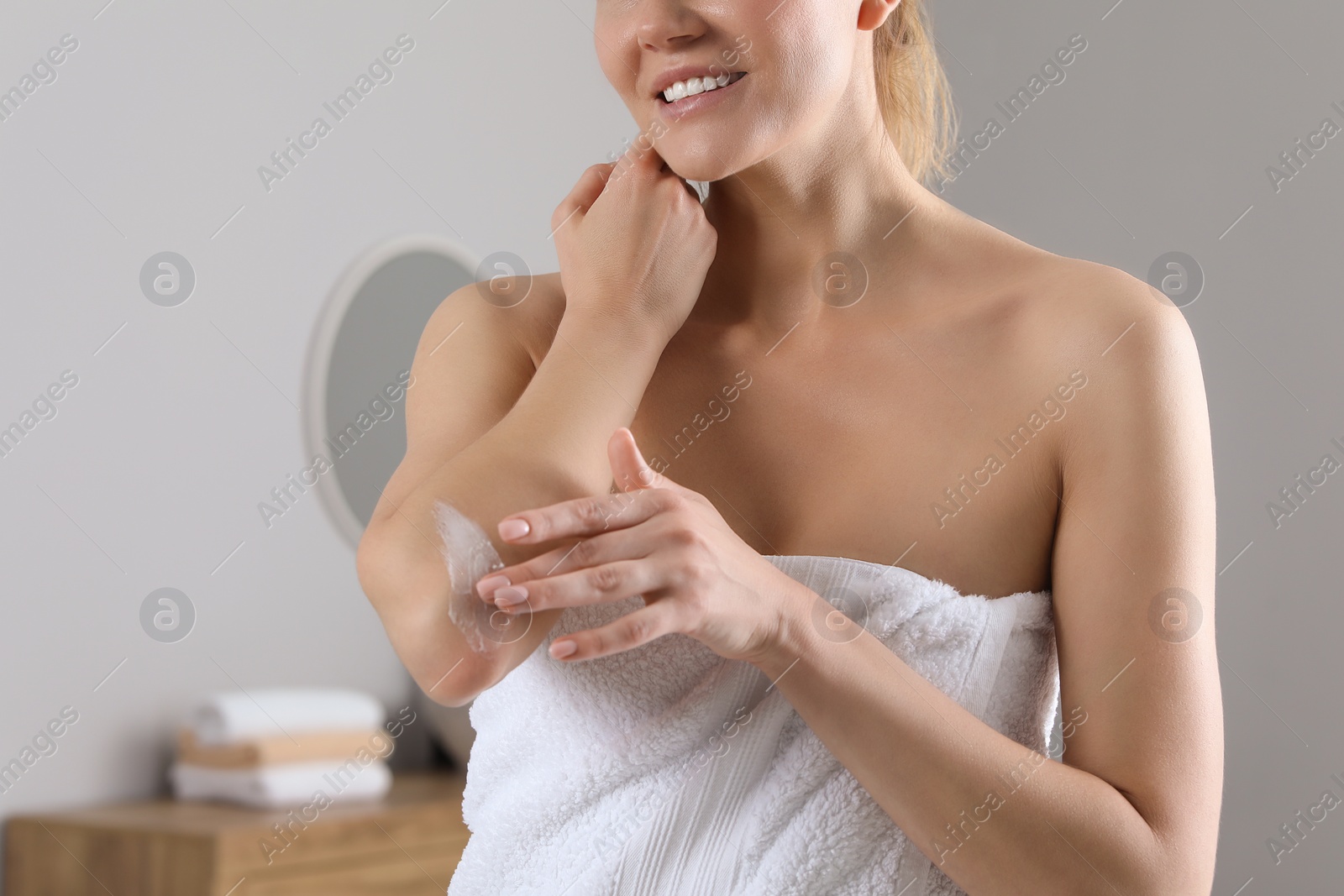 Photo of Woman applying body cream onto elbow in bathroom, closeup. Space for text
