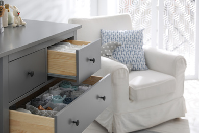 Photo of Modern open chest of drawers with clothes and accessories in baby room