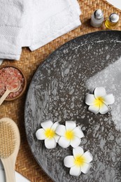 Photo of Bowl of water with plumeria flowers and different spa supplies on table, top view