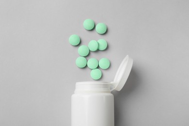 Photo of Light green vitamin pills and bottle on grey background, top view