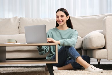 Photo of Happy woman working with laptop at coffee table in living room