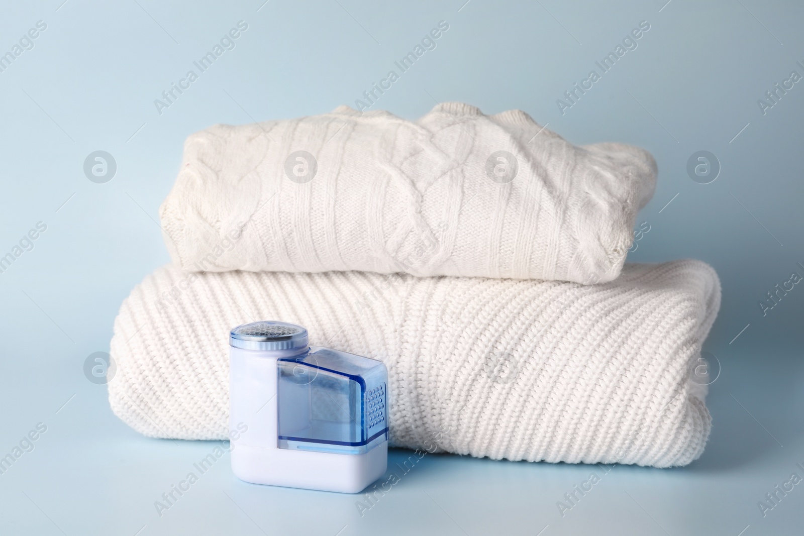 Photo of Modern fabric shaver and knitted clothes on light blue background