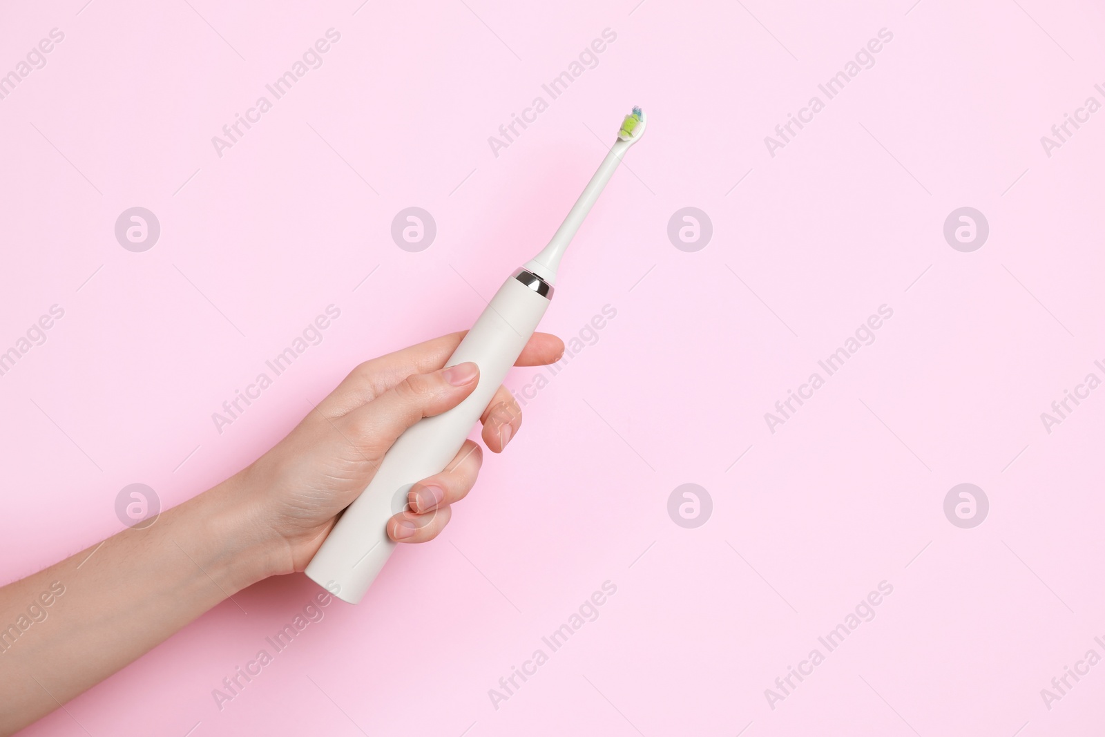 Photo of Woman holding electric toothbrush on pink background, closeup