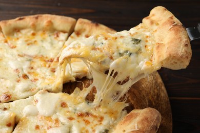 Photo of Taking piece of delicious cheese pizza at wooden table, closeup