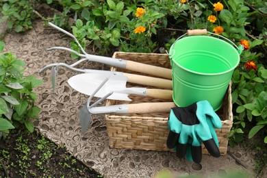 Photo of Wicker basket with gloves, bucket and gardening tools near flowers outdoors
