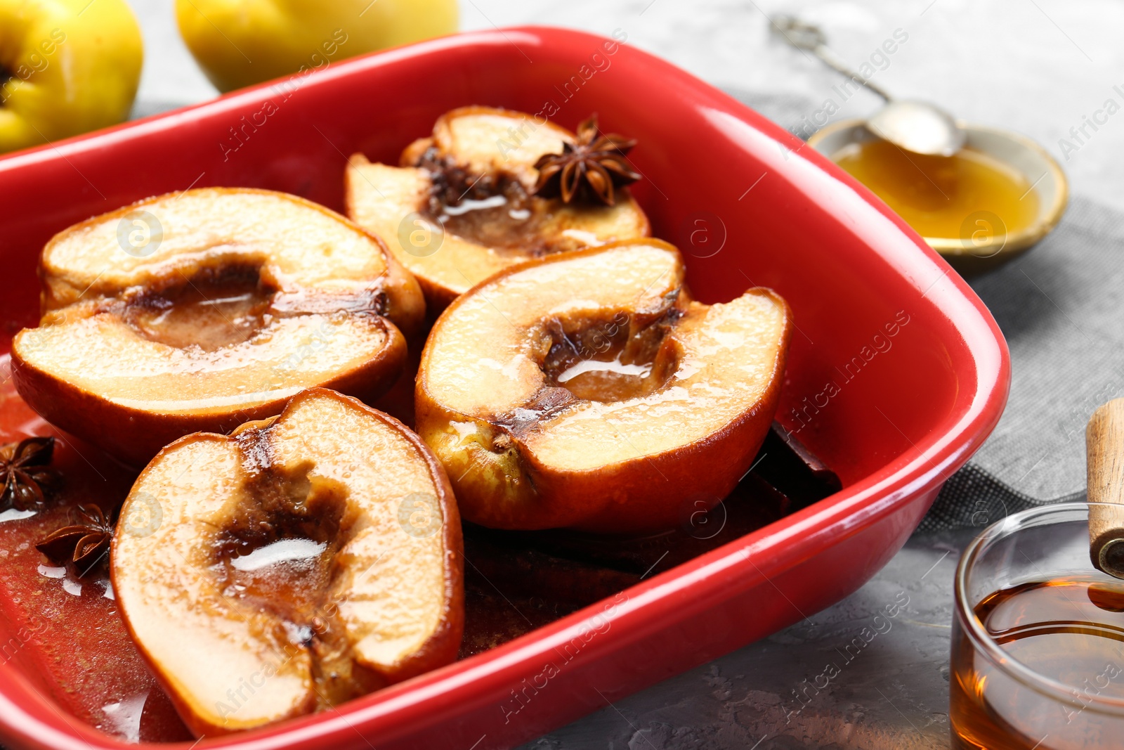 Photo of Tasty baked quinces with honey in dish on grey textured table, closeup