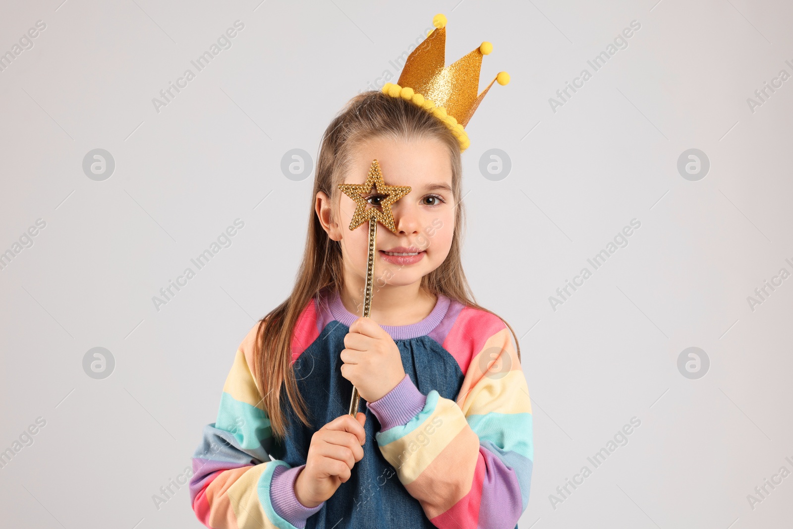 Photo of Cute girl in golden crown with magic wand on light grey background. Little princess