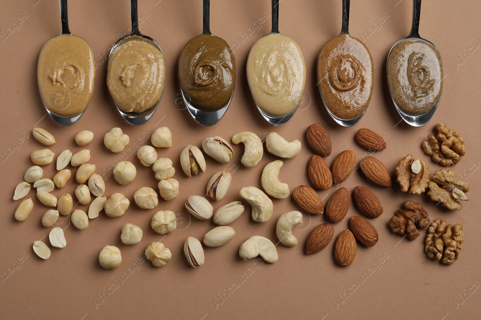 Photo of Tasty nut butters in spoons and raw nuts on light brown table, flat lay