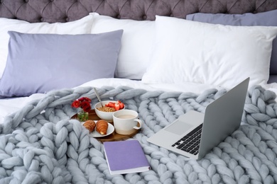 Photo of Laptop, tray with breakfast and notebook on bed. Interior element
