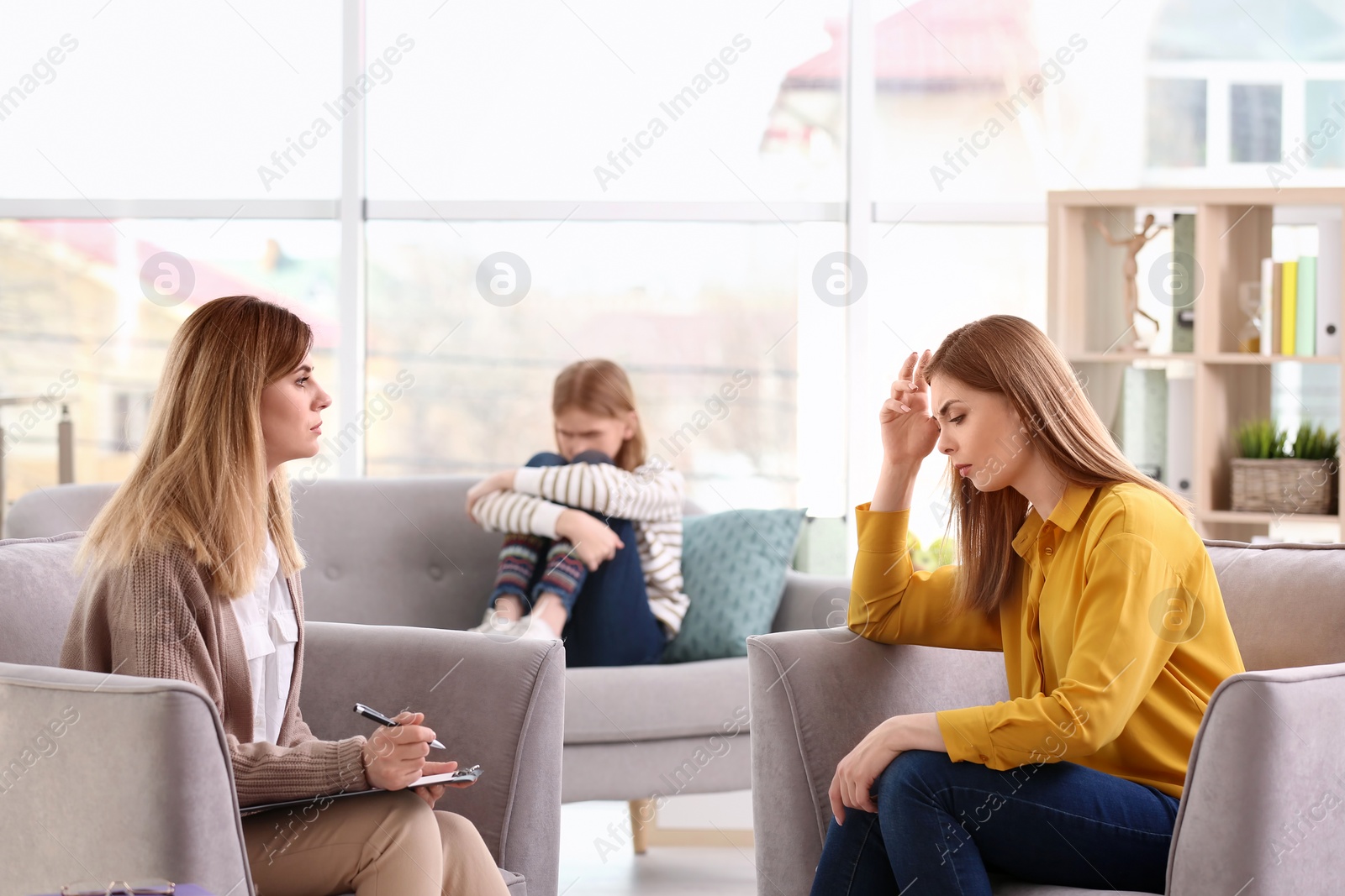 Photo of Young female psychologist working with teenage girl and her mother in office