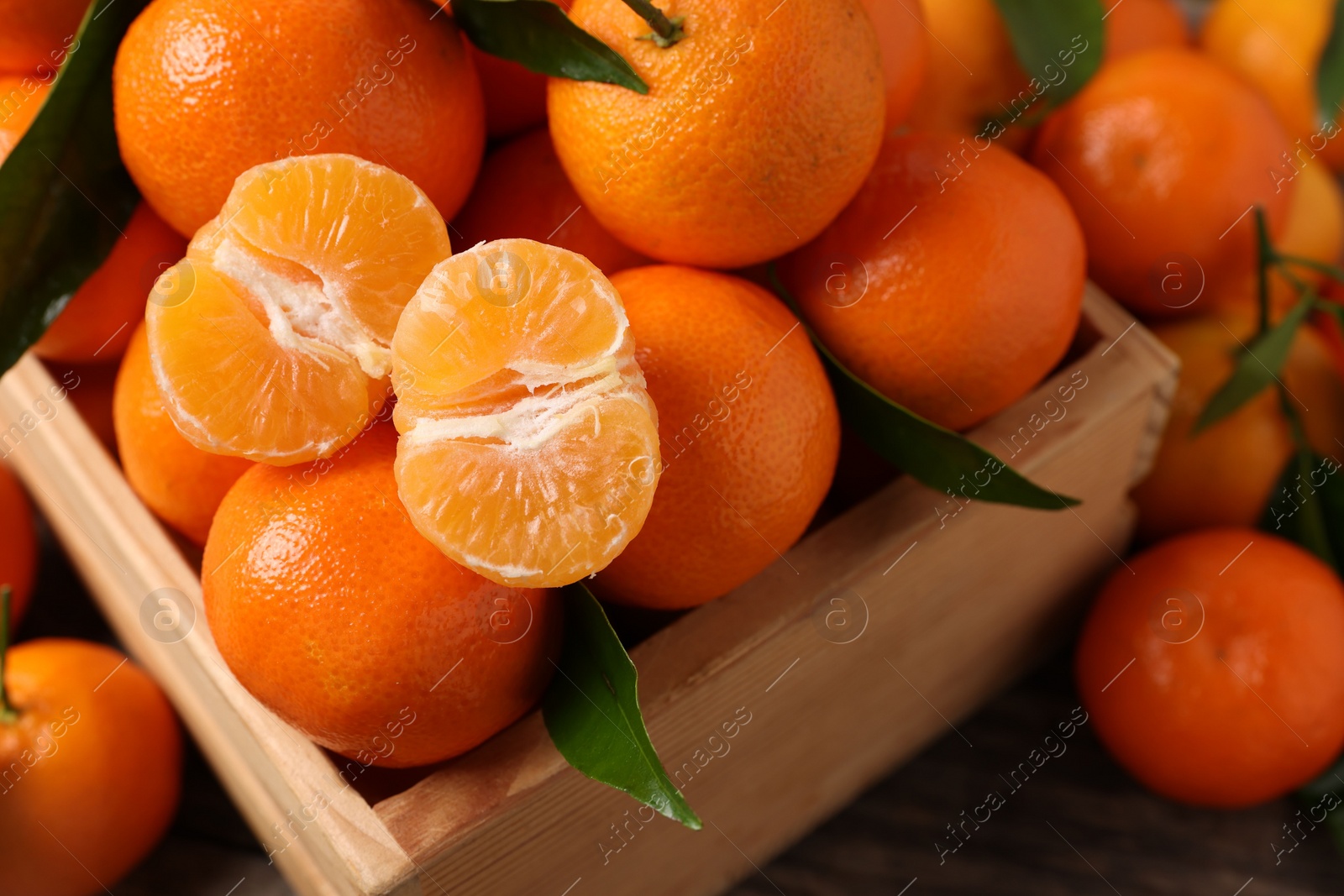 Photo of Delicious tangerines with leaves in crate on table, above view