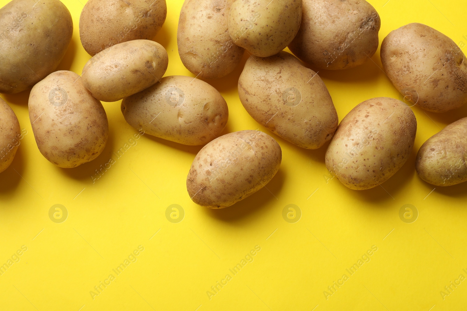 Photo of Many fresh potatoes on yellow background, flat lay. Space for text