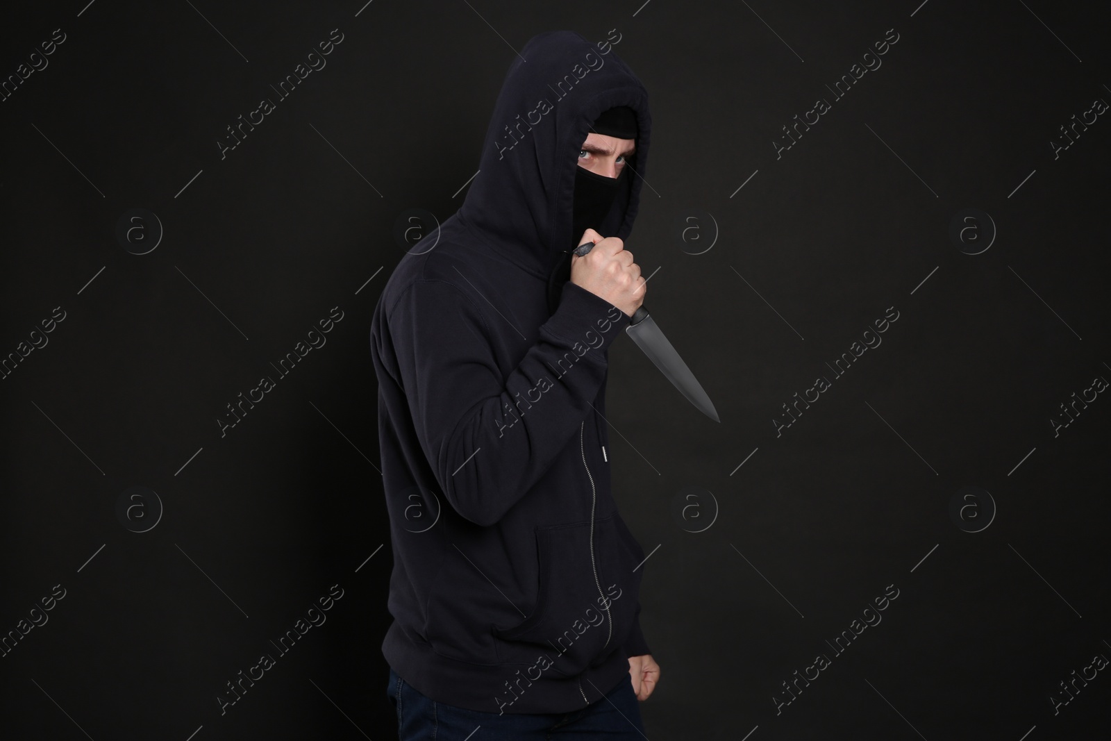 Photo of Man in mask with knife on black background. Dangerous criminal