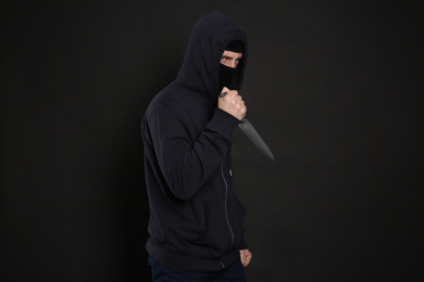 Photo of Man in mask with knife on black background. Dangerous criminal