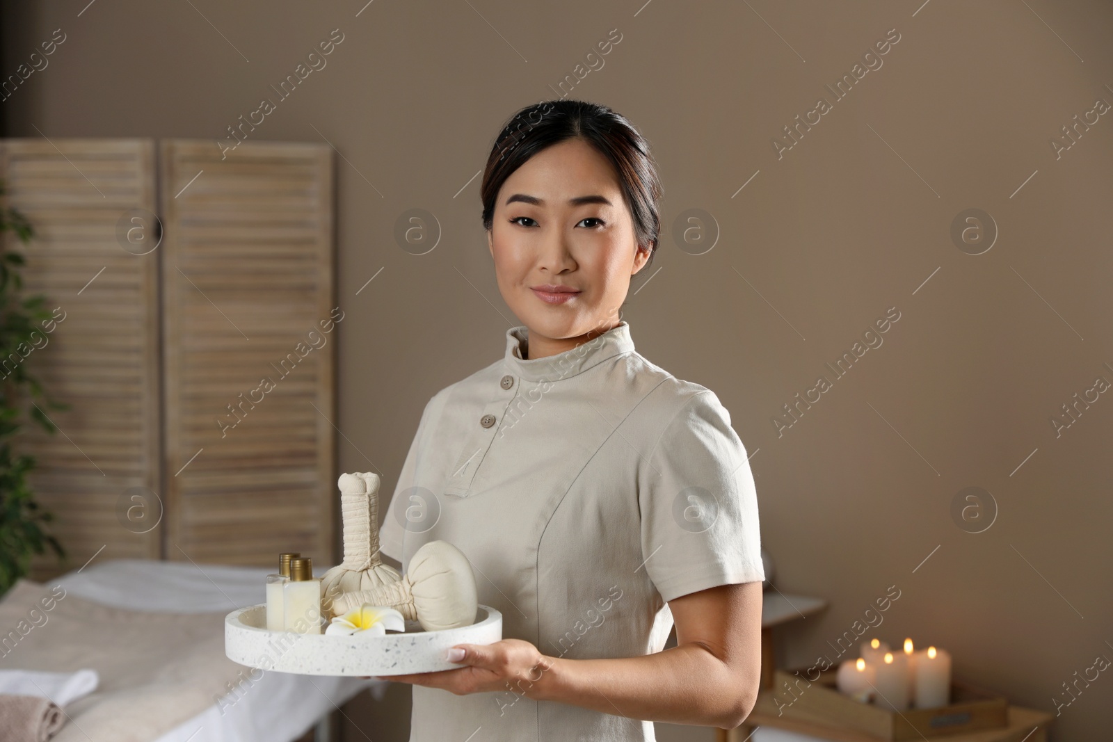 Photo of Portrait of young Asian masseur holding tray with spa stuff in salon