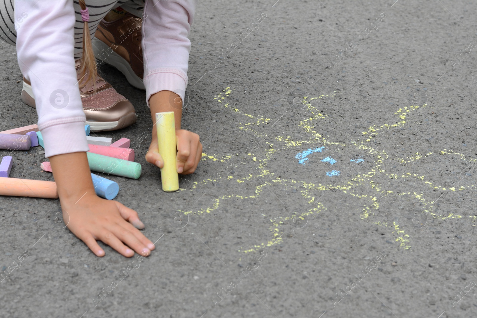 Photo of Little child drawing sun with chalk on asphalt, closeup