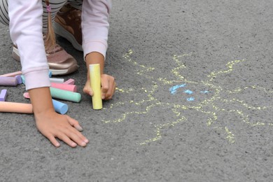 Little child drawing sun with chalk on asphalt, closeup