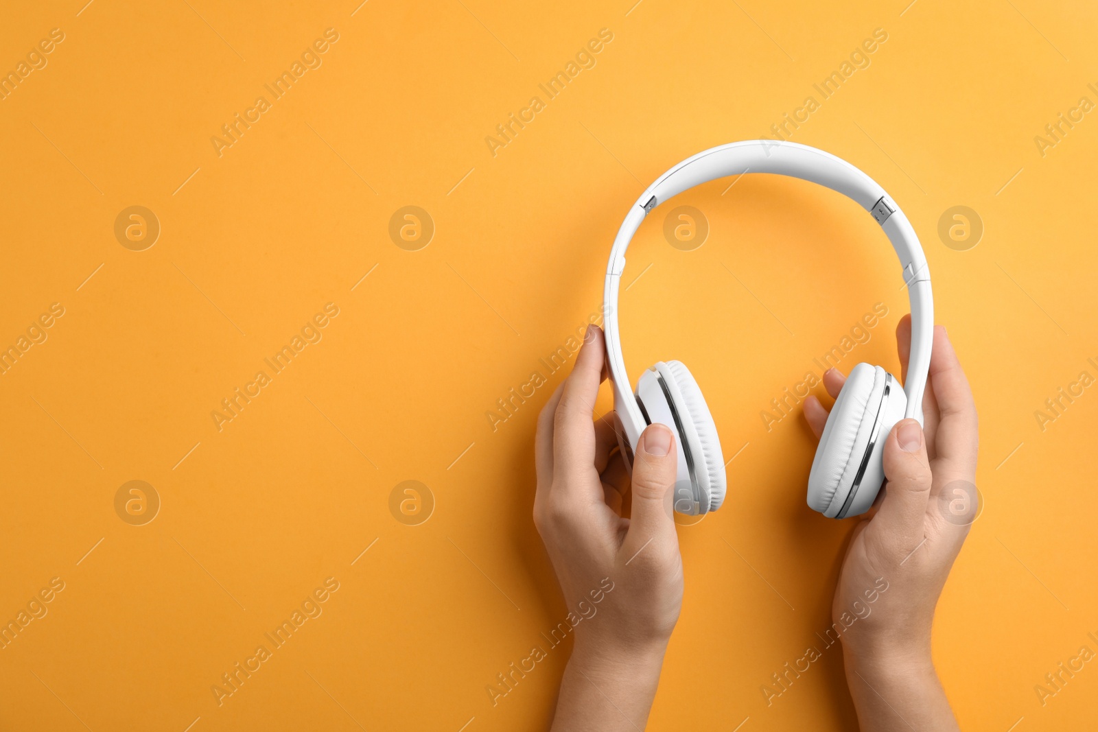 Photo of Woman holding headphones on color background, top view. Space for text