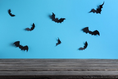 Photo of Empty wooden table near light blue wall decorated with paper bats. Halloween celebration