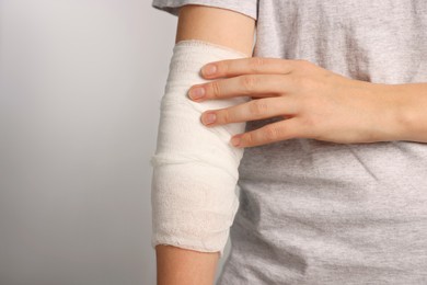 Photo of Woman with arm wrapped in medical bandage on light grey background, closeup. Space for text