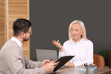 Photo of Man with clipboard and woman at wooden table in office. Manager conducting job interview with applicant