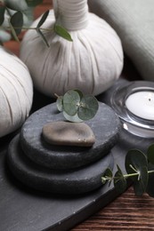 Photo of Beautiful spa composition with herbal massage bags, stones and eucalyptus branches on wooden table, closeup