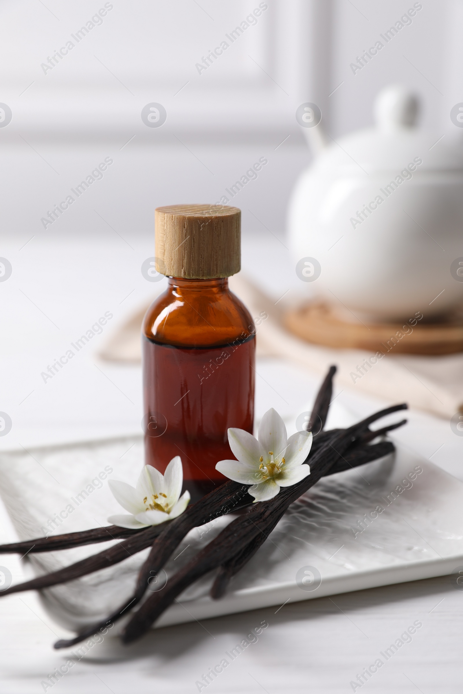 Photo of Vanilla pods, essential oil and flowers on white table