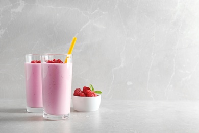 Glasses of tasty smoothie with raspberries on light table. Space for text