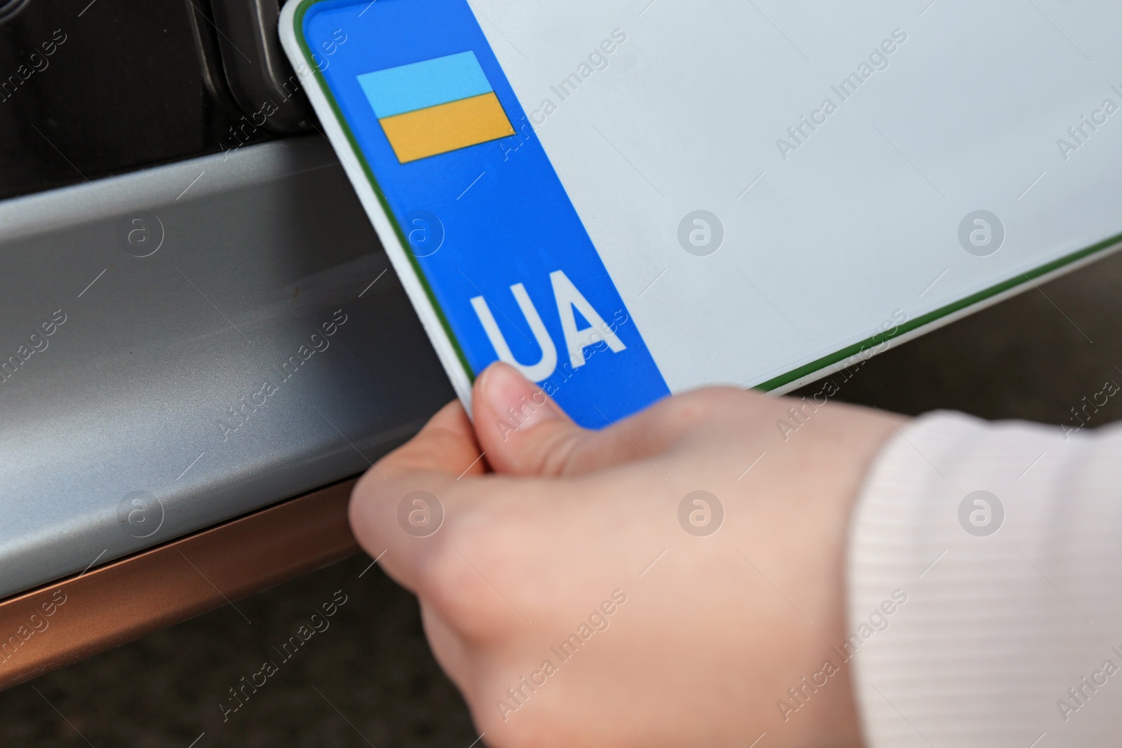 Photo of Woman installing vehicle registration plate, closeup view