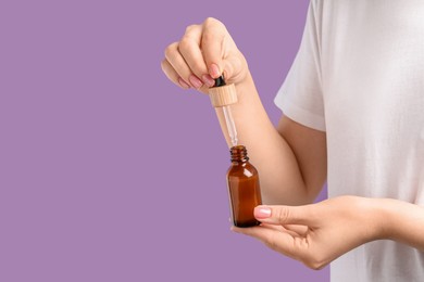 Photo of Woman dripping serum from pipette into bottle against lilac background, closeup. Space for text