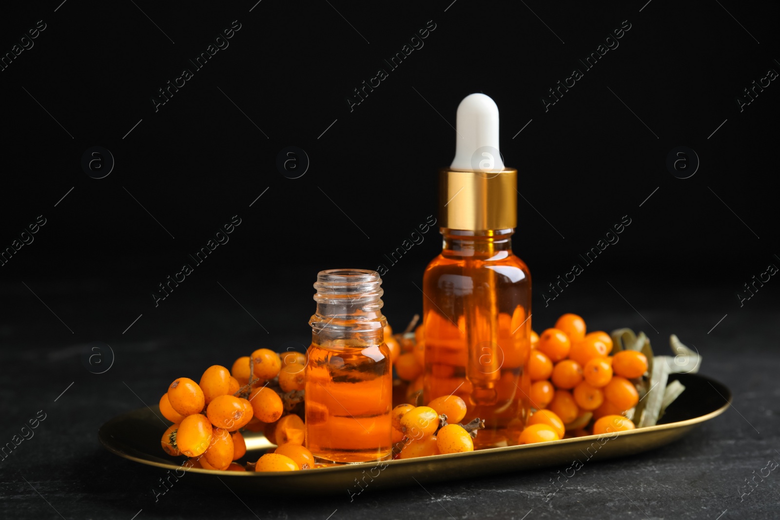 Photo of Ripe sea buckthorn and bottles of essential oil on black table