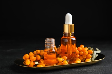 Photo of Ripe sea buckthorn and bottles of essential oil on black table