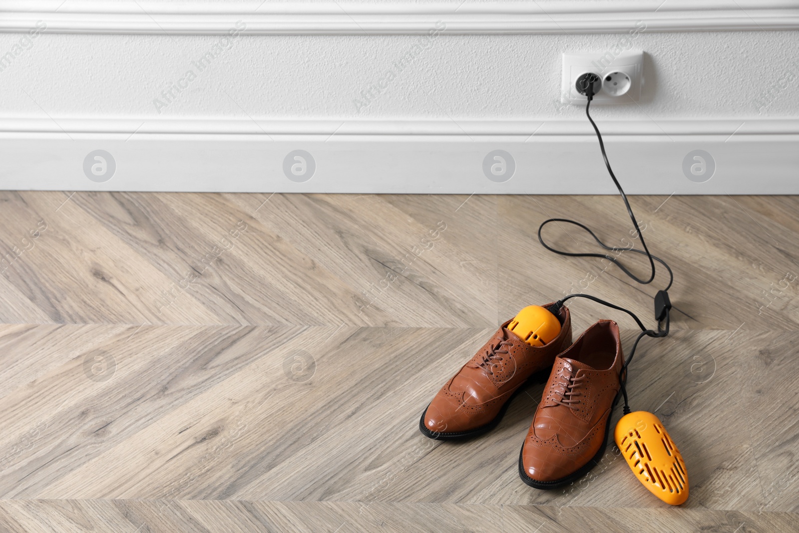 Photo of Pair of stylish shoes with modern electric footwear dryer on floor indoors. Space for text