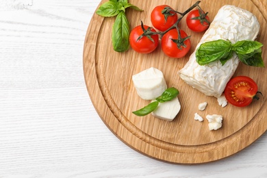 Photo of Delicious goat cheese with basil and tomatoes on white wooden table, top view