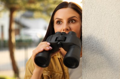 Concept of private life. Curious young woman with binoculars spying on neighbours outdoors