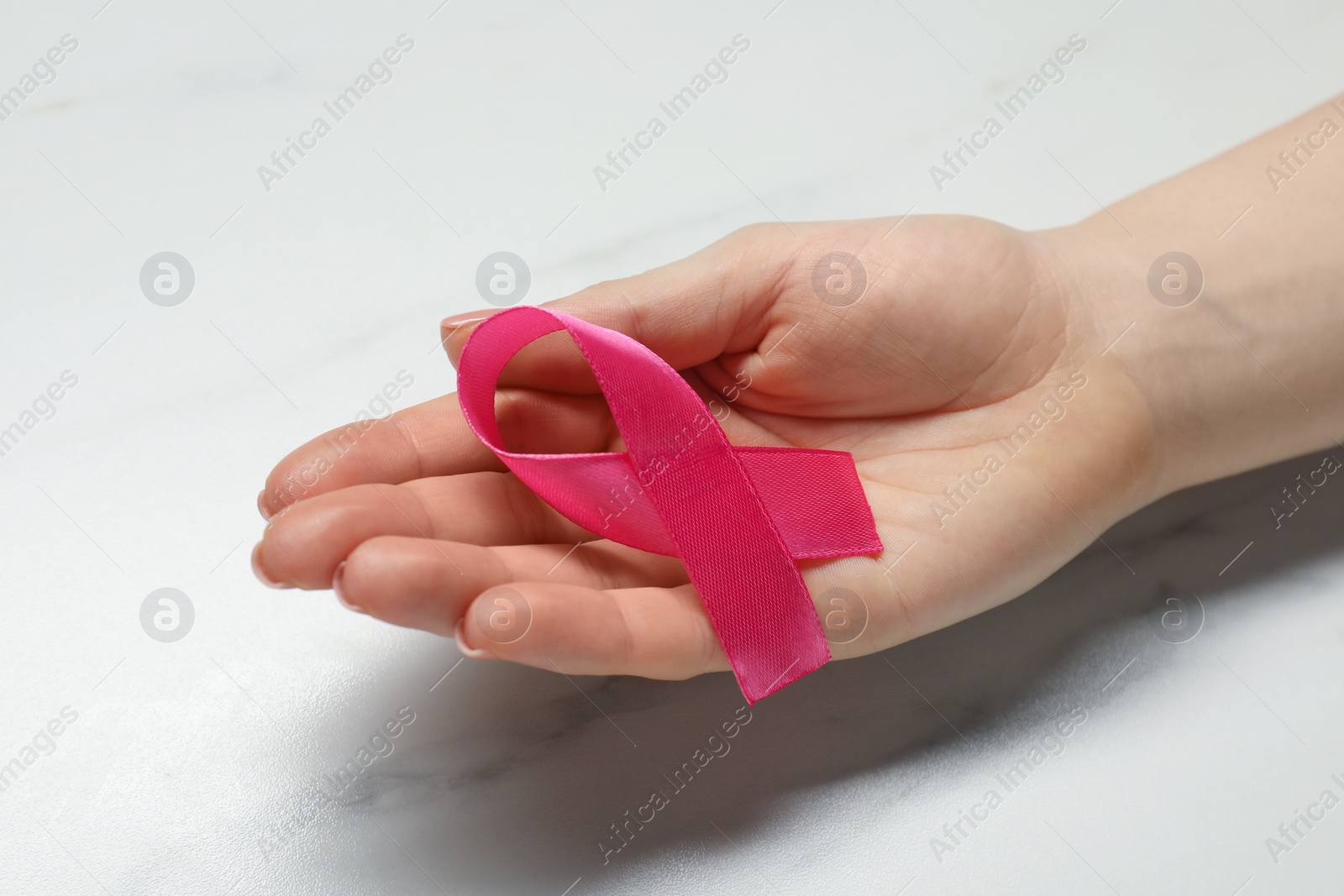 Photo of Woman with pink ribbon at white marble table, closeup. Breast cancer awareness
