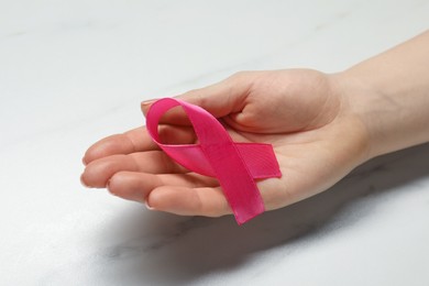 Woman with pink ribbon at white marble table, closeup. Breast cancer awareness