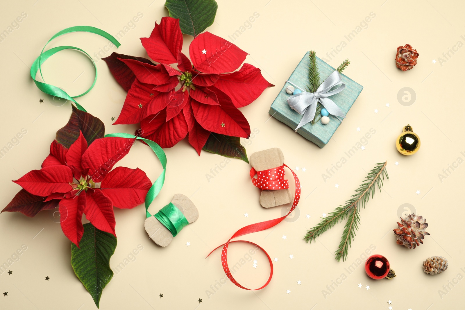 Photo of Flat lay composition with poinsettias (traditional Christmas flowers) and holiday decor on beige background