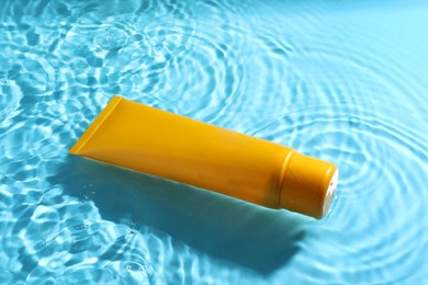 Photo of Tube with moisturizing cream in water on light blue background