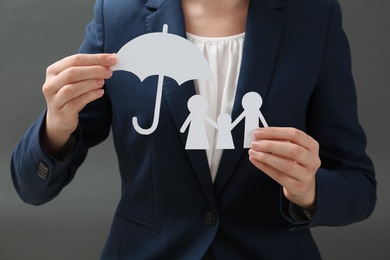 Woman holding cutout paper family and umbrella, closeup. Life insurance concept